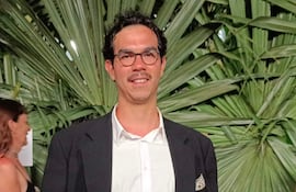 Juanjo Pereira en traje oscuro, feliz y con gafas, en un evento social con una mujer de vestido plateado al fondo.