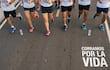 Seis corredores de diferentes edades y géneros en camisetas blancas, corriendo al aire libre, con botellas de agua en el suelo.