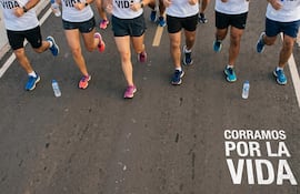 Seis corredores de diferentes edades y géneros en camisetas blancas, corriendo al aire libre, con botellas de agua en el suelo.