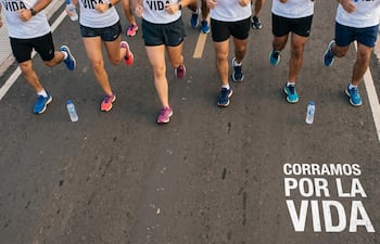 Seis corredores de diferentes edades y géneros en camisetas blancas, corriendo al aire libre, con botellas de agua en el suelo.