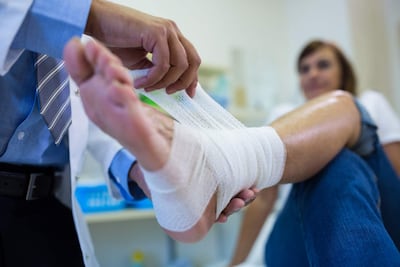 Médico de bata blanca y corbata de rayas atiende a paciente con pie vendado en ambiente limpio y organizado.