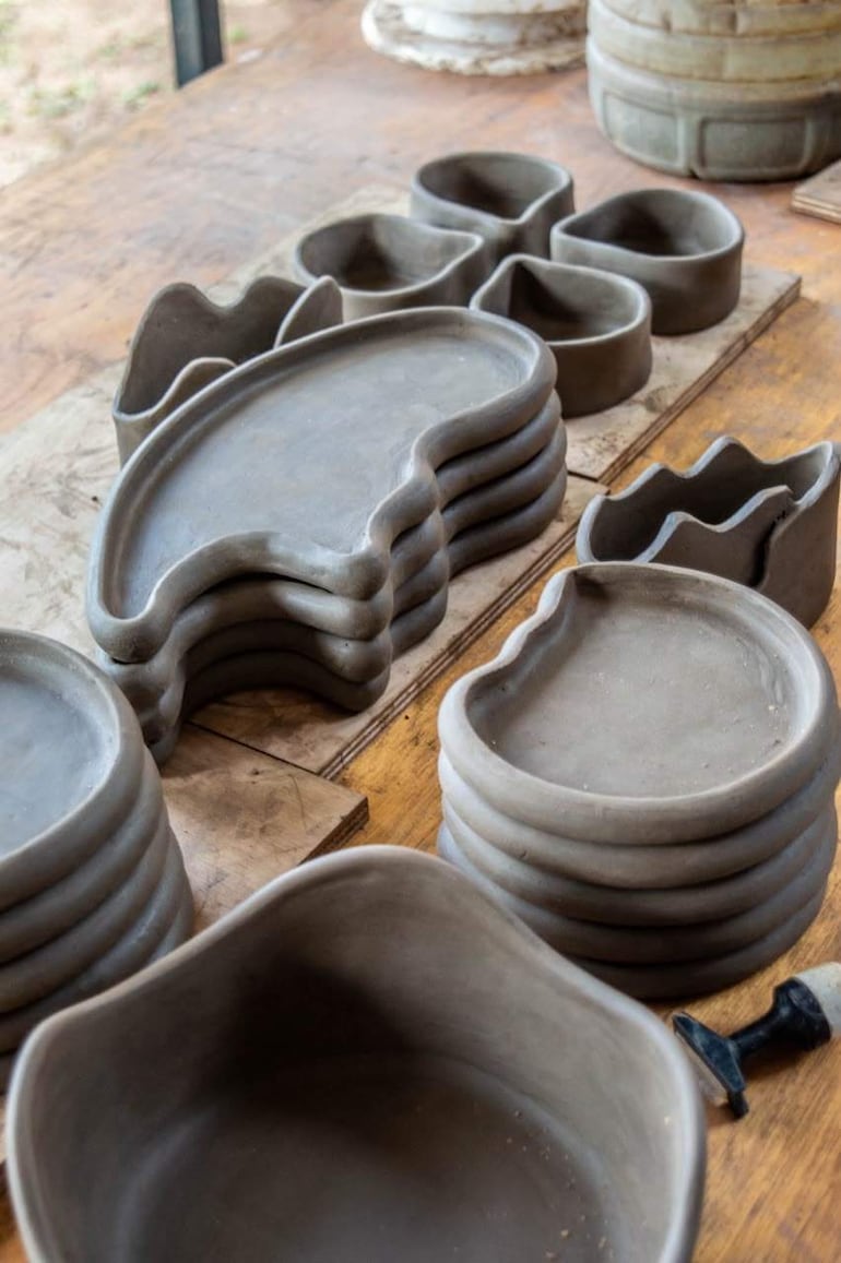 Conjunto de platos y recipientes de cerámica artesanal sobre madera, en tonos grises y de formas irregulares.