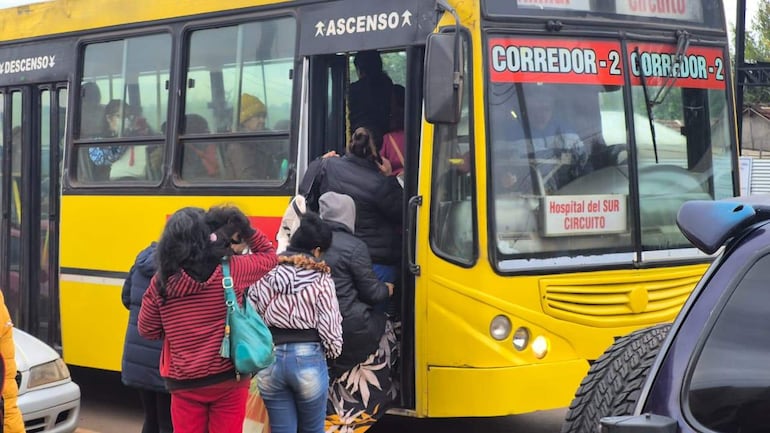 Mujeres con abrigos y mochilas esperan para ingresar a un autobús amarillo en un entorno urbano fresco.