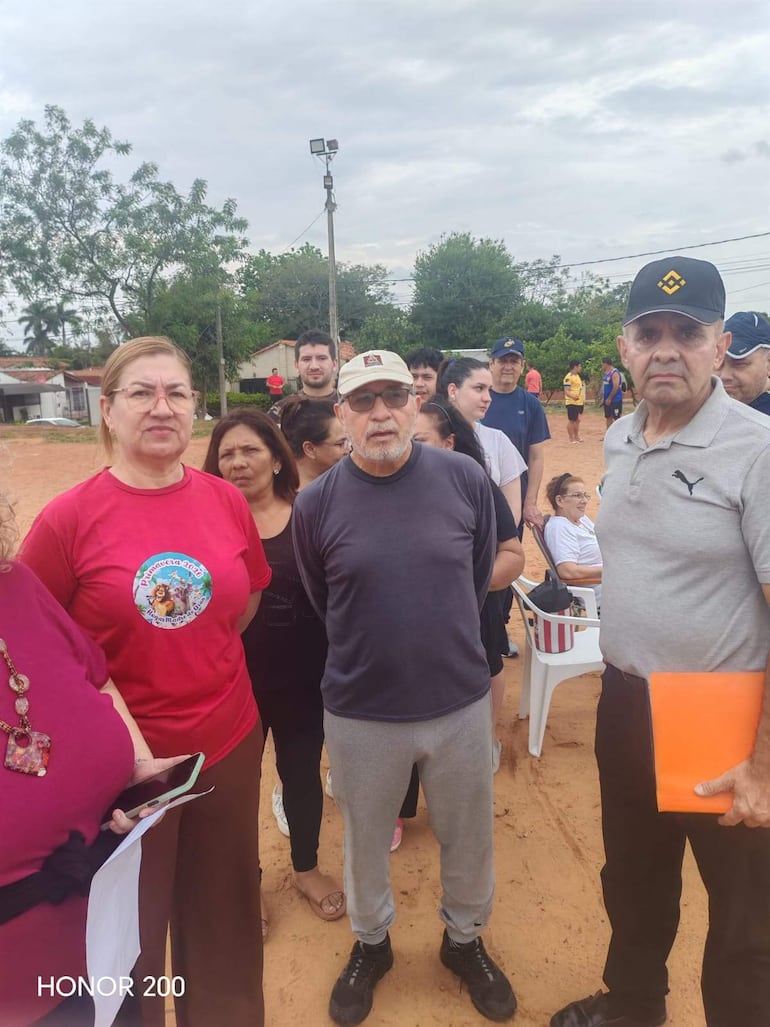 Mujer en camiseta roja y hombre canoso conversan con otros vecinos en un ambiente comunitario al aire libre.