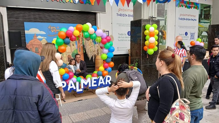 Hombre sonriente junto a una niña en un ambiente festivo decorado con globos. Mujeres y niños disfrutan del evento.