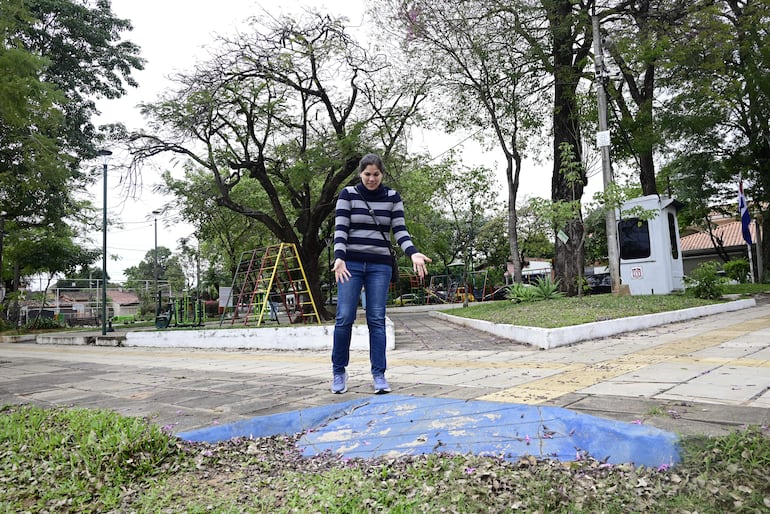Guadalupe Quiñonez de pie en un parque, vistiendo suéter a rayas y jeans, mirando sorprendidamente un área pintada de azul.