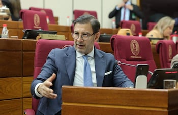 Silvio Ovelar, con traje oscuro y corbata celeste, habla en el Senado, mientras otros senadores lo observan.