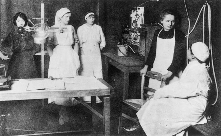 Marie Curie explicando a un médico y un grupo de enfermeras los beneficios de la radioterapia.