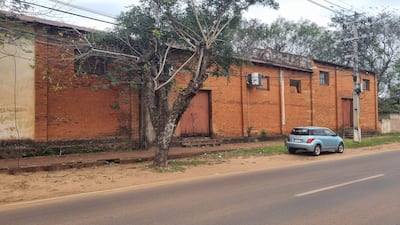 Calle desierta con un vehículo celeste estacionado junto a un edificio antiguo de ladrillo y un árbol.