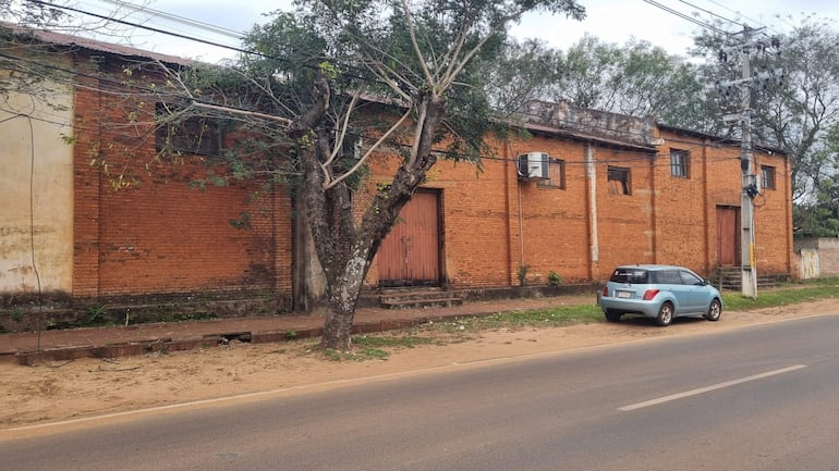 Calle desierta con un vehículo celeste estacionado junto a un edificio antiguo de ladrillo y un árbol.