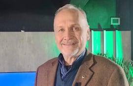 Mario Ferreiro sonríe con abrigo marrón y suéter azul en un estudio de televisión, con el logo de Doble B de fondo.