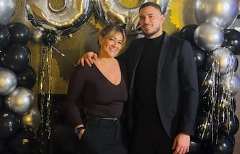 Antonio Sanabria en traje oscuro y mujer con blusa y falda negra sonríen en celebración, rodeados de globos y decoraciones festivas.