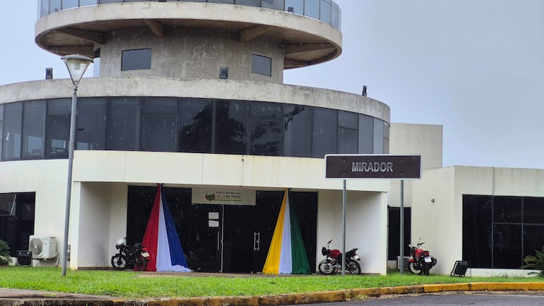 Edificio moderno del Mirador Junta Municipal de Cambyretá con drapeados en rojo, azul y amarillo; cielos nublados y motocicletas estacionadas.