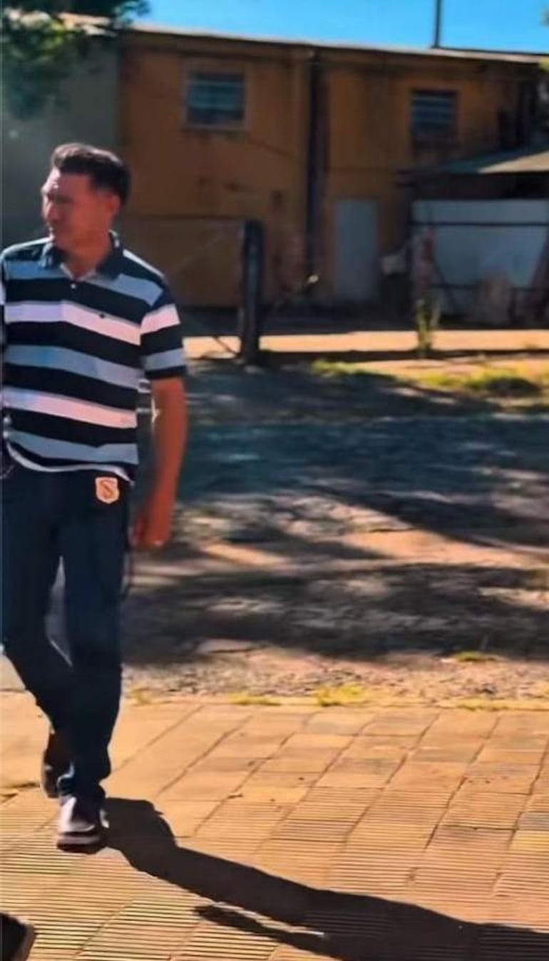 Jhonatan Giles en camiseta de rayas azules y blancas, caminando en un área con edificios de fondo y sin otras personas visibles.