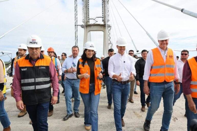 Santiago Peña y Claudia Centurión en el puente, vestidos con chalecos reflectantes y cascos, conversando con gestos de aprobación.
