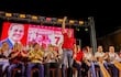 Mario Abdo Benítez de pie con camiseta roja, levantando la mano y sonriendo mientras otros aplauden en un mitin político.
