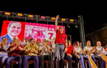 Mario Abdo Benítez de pie con camiseta roja, levantando la mano y sonriendo mientras otros aplauden en un mitin político.