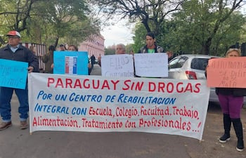 Seis manifestantes sostienen pancartas y carteles enérgicos, vestimenta variada, expresiones de determinación y seriedad en un entorno urbano.