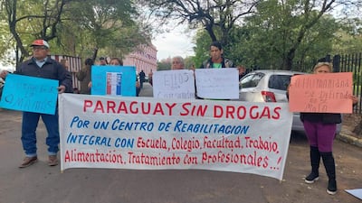 Seis manifestantes sostienen pancartas y carteles enérgicos, vestimenta variada, expresiones de determinación y seriedad en un entorno urbano.