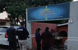 Grupo de cuatro personas, incluido un policía con chaqueta, conversan frente a la funeraria Alto Paraná en un ambiente tenso.