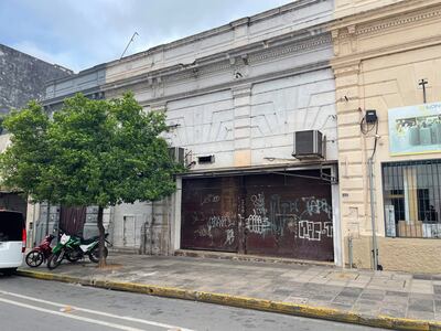 Furgoneta negra y dos motocicletas estacionadas en calles vacías, con edificios blancos desgastados y grafitis en las paredes.