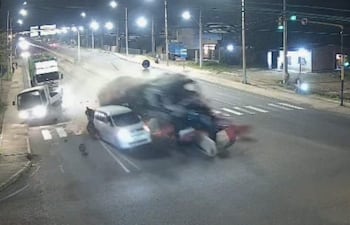 Accidente nocturno en carretera, camión colisiona con automóvil, nube de polvo y escombros en el impacto.