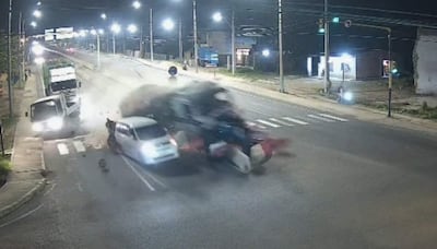 Accidente nocturno en carretera, camión colisiona con automóvil, nube de polvo y escombros en el impacto.