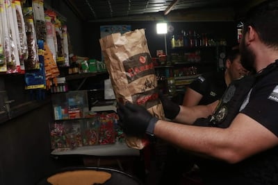 Agente en uniforme y guantes sostiene paquete de 'CARBON' en kisko. Estanterías con productos al fondo.