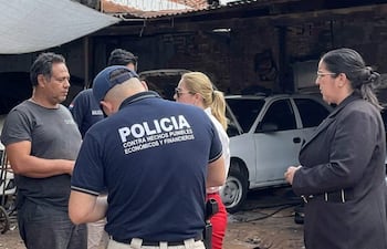 Luis Alberto Quintana Acosta en taller mecánico con un policía y dos mujeres en conversación.