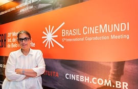 Paz Encina, con camisa blanca y gafas, presenta una expresión de felicidad en un evento de cine con un cartel de fondo.