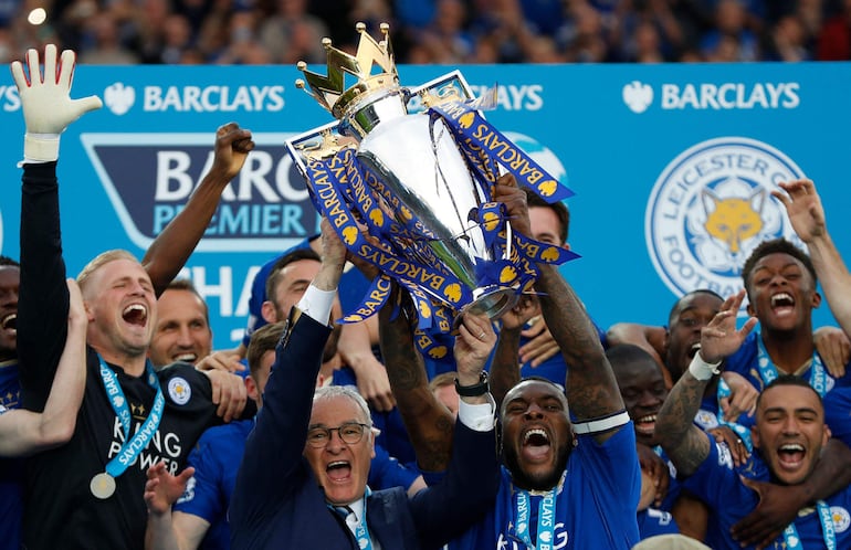 El entrenador italiano del Leicester City, Claudio Ranieri (C), y el defensor inglés del Leicester City, Wes Morgan, levantan el trofeo de la Premier League tras ganar el campeonato y el partido de fútbol de la Premier League inglesa en 2016.