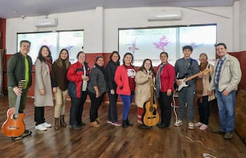 Doce personas, principalmente mujeres, en un salón luminoso, algunas con guitarras, expresan felicidad durante una actividad musical interactiva.