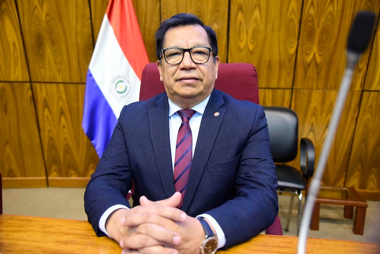 Tadeo Rojas, vestido con traje oscuro y gafas, sentado en silla formal, con la bandera de Paraguay de fondo.