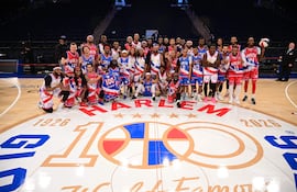 Grupo de 30 Globetrotters sonríen en cancha, vestidos con colores vibrantes y el logo del equipo en el suelo.