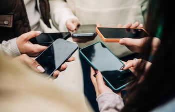 Manos de diversas personas sosteniendo teléfonos móviles de distintos colores y diseños en un entorno informal.