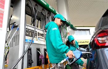 Dos empleados en uniformes verdes trabajan en dispensador de combustible en estación Petrobras, uno sostiene manguera.