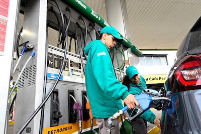 Dos empleados en uniformes verdes trabajan en dispensador de combustible en estación Petrobras, uno sostiene manguera.