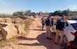 Seis policías en camino de tierra, uno hablando con otro cerca de un vehículo de la policía, excavadora trabajando al fondo.