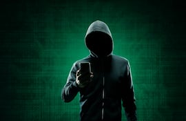 Un hombre con capucha y un teléfono celular en la mano.