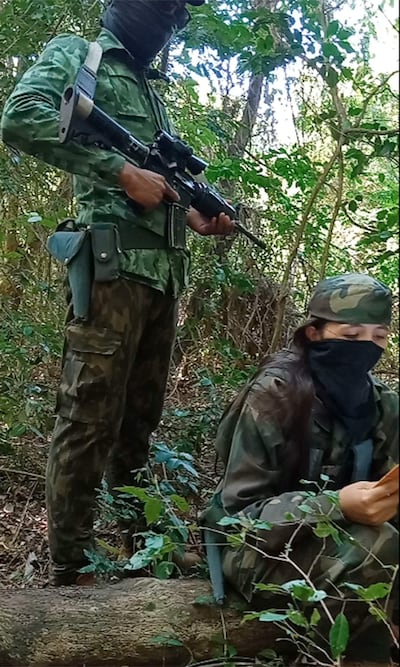 Lourdes Teresita Ramos Ramírez sentada en tronco, con rostro cubierto, junto a otro individuo armado en un entorno selvático.