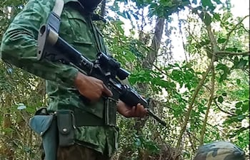 Lourdes Teresita Ramos Ramírez sentada en tronco, con rostro cubierto, junto a otro individuo armado en un entorno selvático.