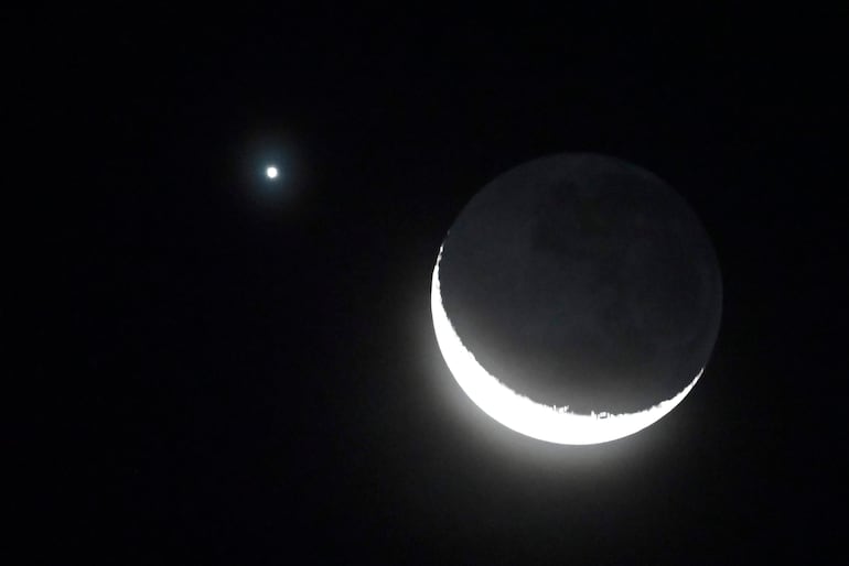 Luna creciente iluminada en un cielo oscuro, acompañada por un planeta brillante, creando un espectáculo astronómico sereno.
