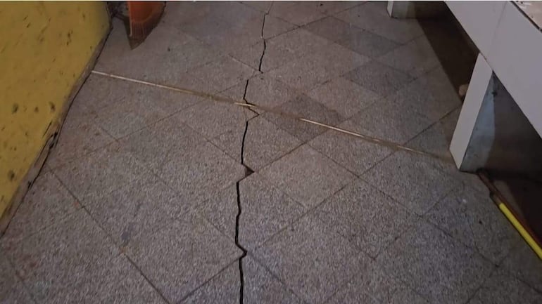 Suelo de baldosas agrietado, con parte de un utensilio de limpieza visible en el borde derecho.