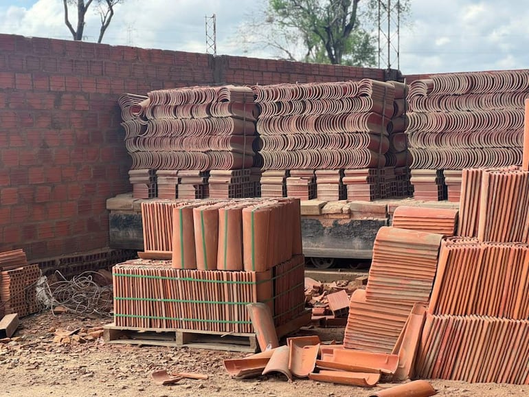 Depósito de materiales de construcción con pilas de tejas y ladrillos en un ambiente exterior iluminado por luz natural.