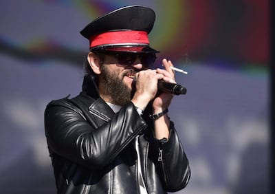 Cantante de Pornostars con chaqueta de cuero negra y gorro militar en el escenario, sosteniendo un micrófono y un cigarrillo, ante un fondo colorido.