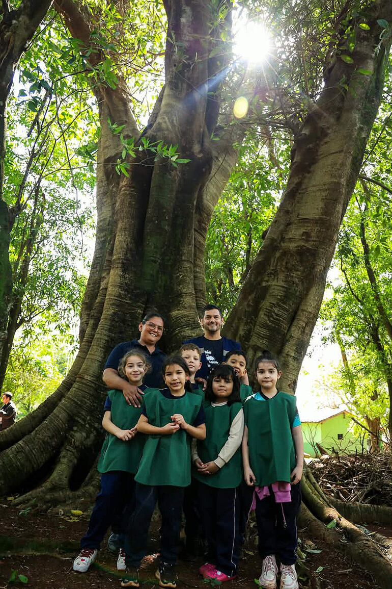 Niños y adultos sonríen en la jungla, vistiendo camisetas verdes y pantalones oscuros, rodeados de vegetación frondosa.