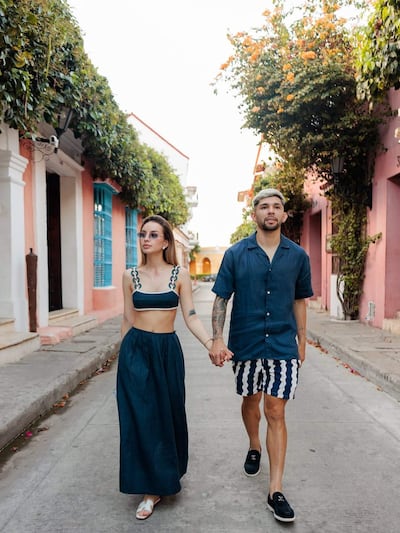 Julio Enciso y Ramón Sosa caminando de la mano, luciendo atuendos casuales y relajados en un entorno de fachadas color pastel.