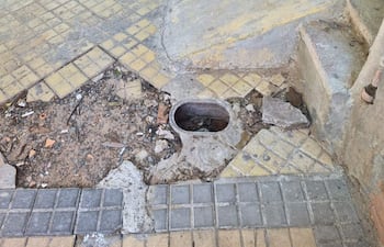 Vereda con hueco significativo, baldosas amarillas y grises, ambiente urbano descuidado.