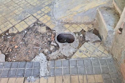 Vereda con hueco significativo, baldosas amarillas y grises, ambiente urbano descuidado.