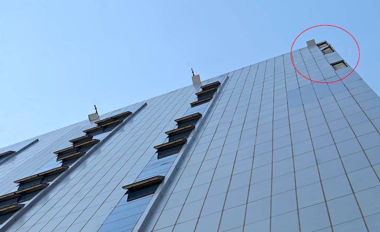 Edificio alto con fachada de vidrio reflejando el cielo despejado, sin personas visibles en el entorno soleado.